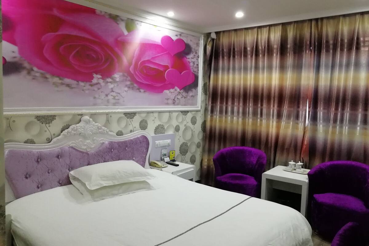 Une chambre d’hôtel avec un grand lit, une table de chevet, un téléphone et deux fauteuils violets.