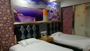 Una habitación de hotel con dos camas individuales, un cabecero con diseño de rombos, una mesita de noche con lámpara y un cuadro grande con una escena costera.