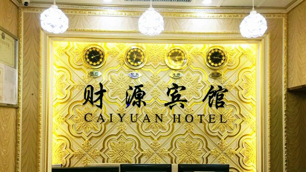 Mostrador de recepción en el Hotel Caiyuan, con una pared decorativa dorada y relojes que marcan diferentes ciudades.