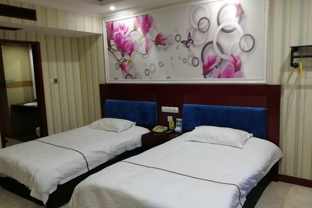 Une chambre d’hôtel avec deux lits, une grande œuvre d’art à motifs floraux accrochée au mur et un miroir.