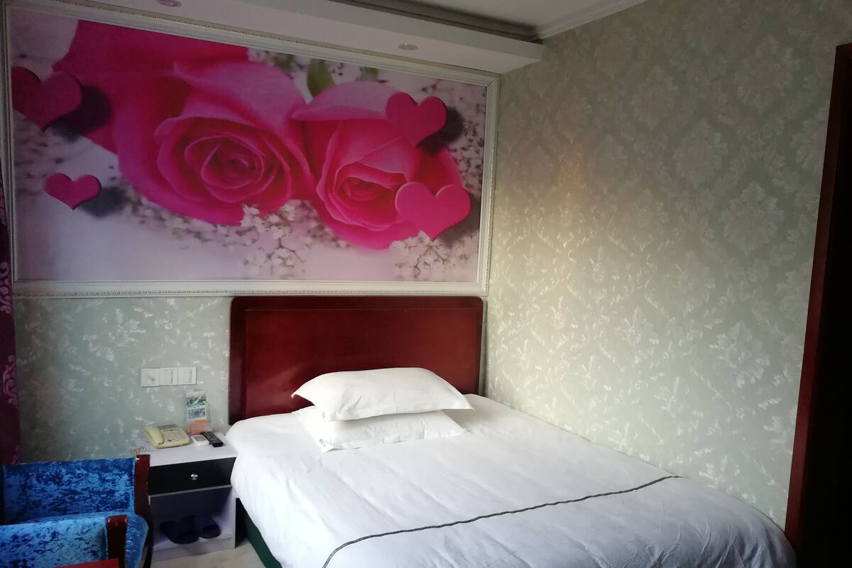 Une chambre d’hôtel avec un lit, une table de chevet, une chaise et un mur orné d’un motif floral.