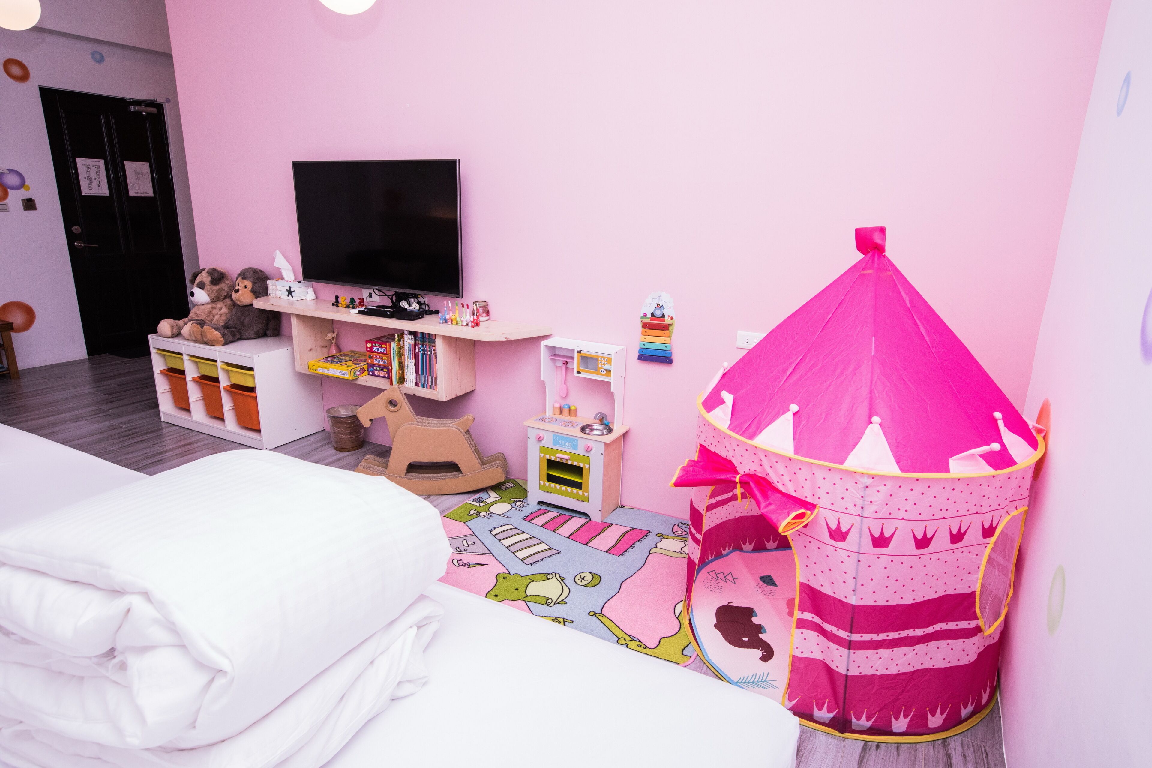Een kinderkamer met een bed, een roze sprookjestent, een televisie en een klein boekenrek.