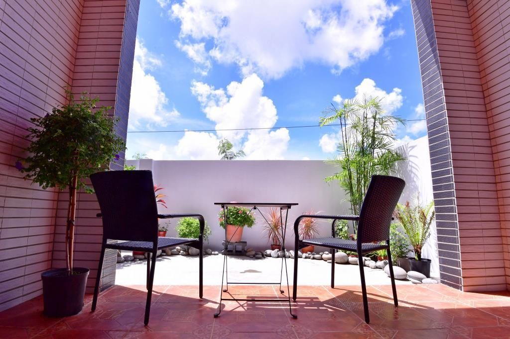 A patio with two black chairs and a small table, surrounded by potted plants and a white wall.
