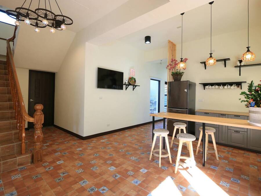 A modern kitchen with a wooden staircase, a TV mounted on the wall, and a refrigerator.