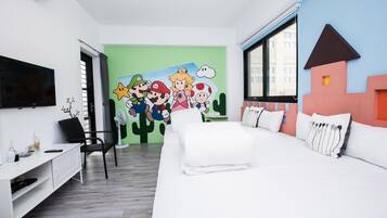A hotel room with a bed, a desk, a chair, a TV, and a mural with cartoon characters.