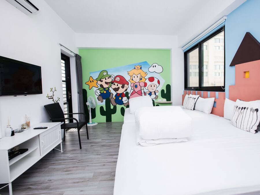 A hotel room with a bed, a desk, a chair, a TV, and a mural with cartoon characters.