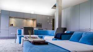 A modern bedroom with a large bed, a seating area, and a kitchenette.