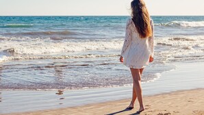 Una persona de pie en la playa, con olas al fondo.
