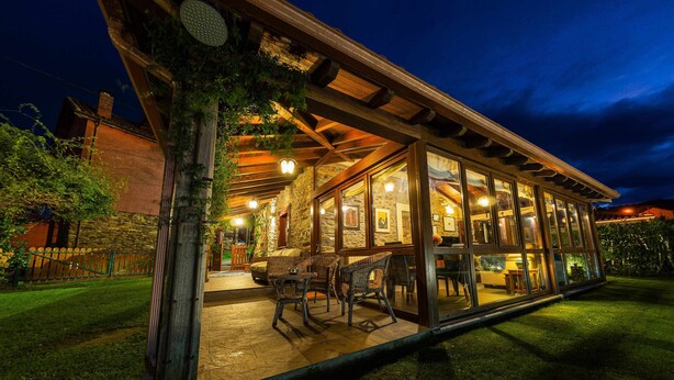 Een glazen gebouw met een terras, zitplaatsen buiten en een gevel van natuursteen.