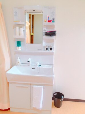 Une salle de bain avec un lavabo blanc, un miroir, un porte-serviettes et une petite étagère contenant des articles de toilette.