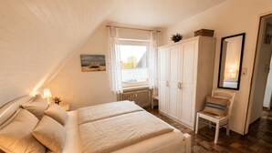 A bedroom with a bed, a chair, a wardrobe, a window, and a painting. - Top vacation home,7 p.,sauna,2 baths,WLAN,fireplace,beach kitchen,terrace,dog,playground (Dornum)