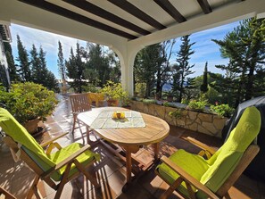 An outdoor patio with a round table and chairs, surrounded by potted plants and a stone wall.