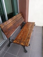 A wooden bench with metal legs, positioned on a tiled floor near a glass door and a wall.