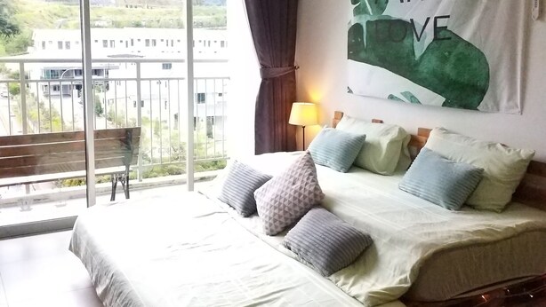 A bedroom with a large bed, multiple pillows, a nightstand, a lamp, and a view of a building and hills through a window. - Misty Forest II - 9 Pax Next To Night Market (Tanah Rata)