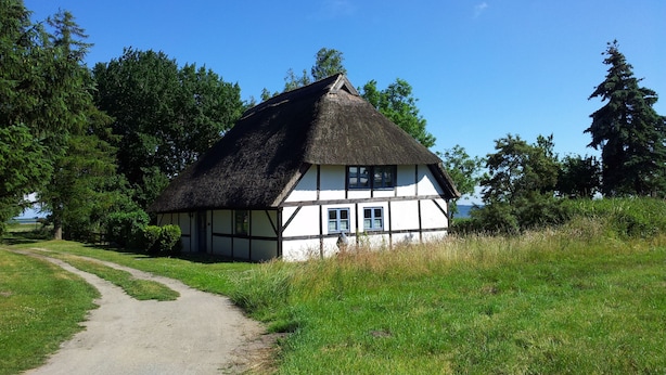 A traditional thatched-roof house with a white exterior and dark wooden beams, surrounded by a grassy field and trees. - The best time on the largest island of Germany enjoy. (Ummanz/Waase)