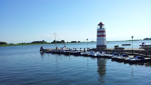 A lighthouse with a red and white striped tower, docked boats, and calm water. - The best time on the largest island of Germany enjoy. (Ummanz/Waase)
