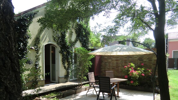 A patio with a table and chairs, surrounded by greenery and a brick wall.