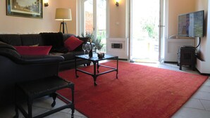 A living room with a black sofa, red cushions, a coffee table, and a red carpet. There is a painting on the wall, a lamp, and a television on a stand.