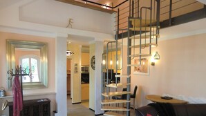 A spacious living area with a staircase, a dining table, and a black leather sofa.