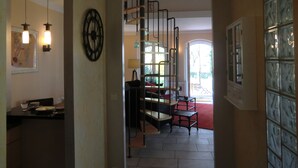 A hallway with a staircase, a dining area with a table and chairs, and a wall with a decorative clock.
