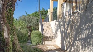 Un étroit sentier menant à un bâtiment doté d’un escalier en pierre et d’une rambarde en métal.