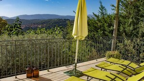 Une terrasse dotée de chaises longues jaunes et d’un parasol jaune, offrant une vue sur un paysage montagneux.
