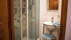 Une salle de bain avec une douche à parois de verre, un lavabo blanc avec une serviette bleue, et un meuble en bois placé au-dessus du miroir.