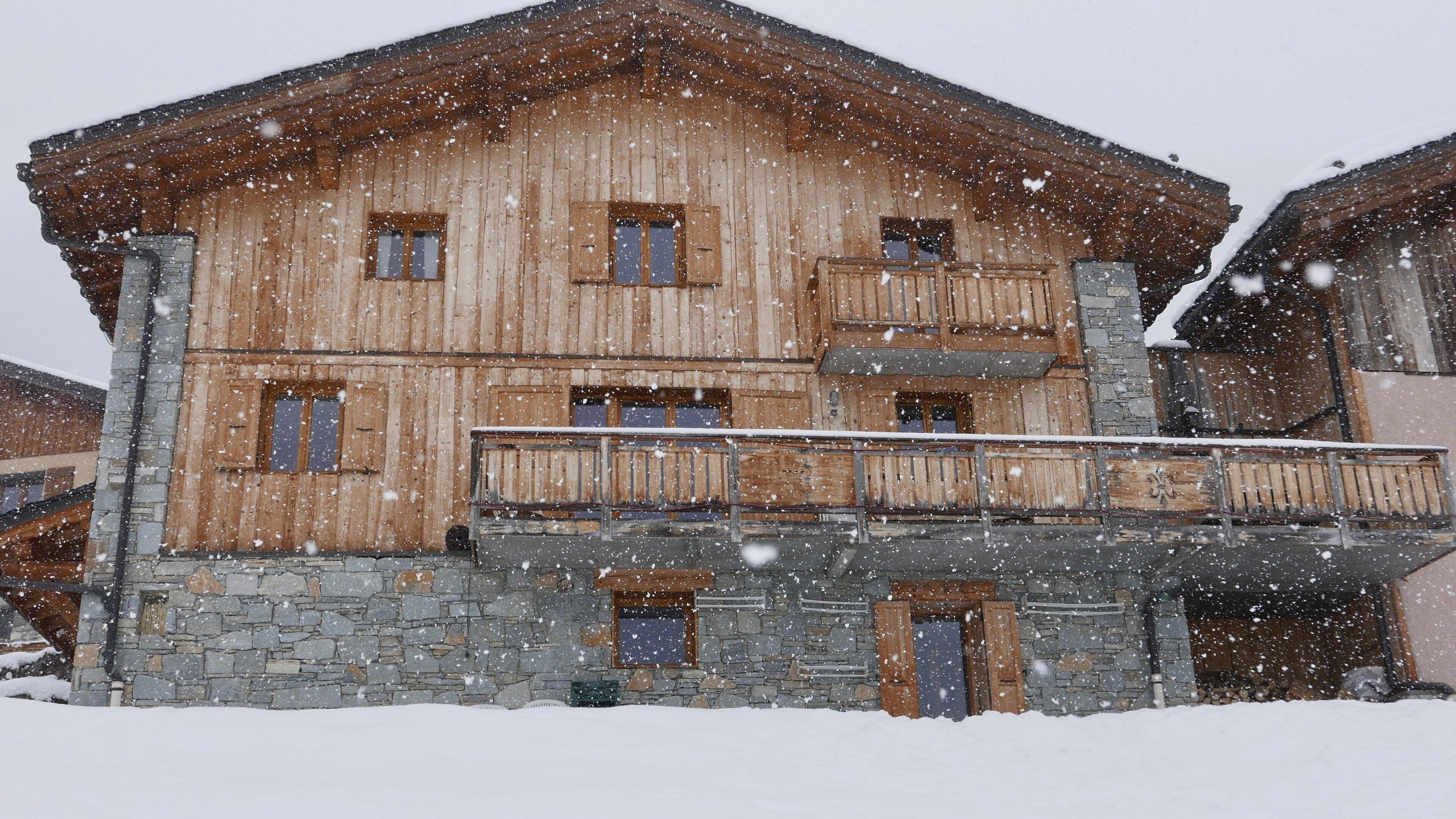 A wooden chalet with a stone foundation, multiple windows, and a balcony.