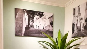 Una poltrona a dondolo con seduta e schienale intrecciati, una pianta in vaso e due fotografie in bianco e nero appese al muro.