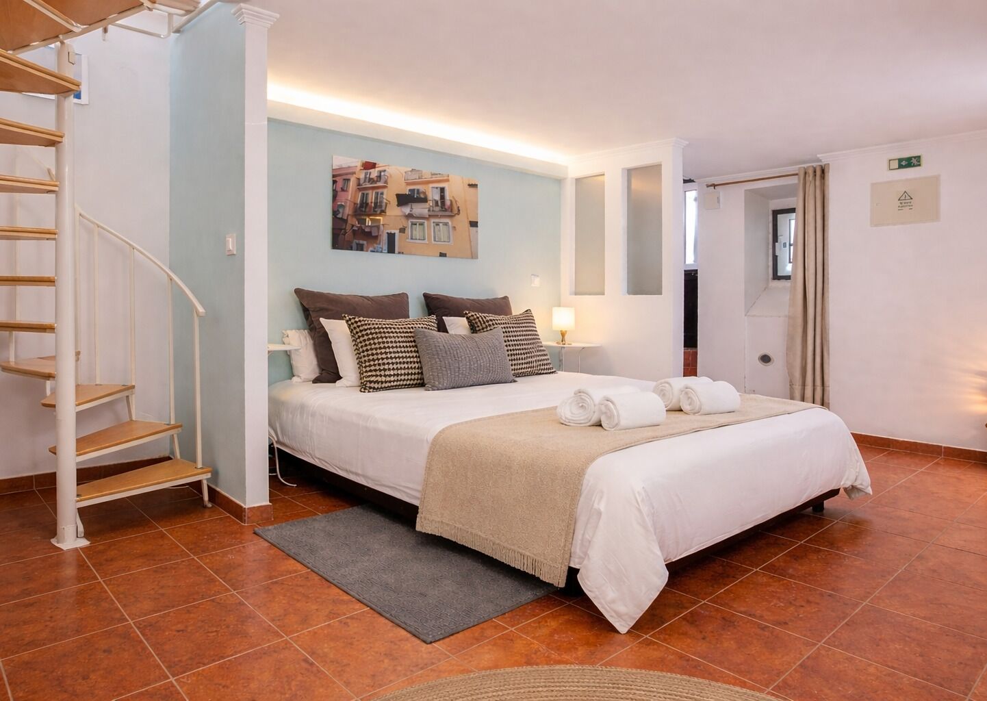 Ein Schlafzimmer mit Bett, Treppe, Wandbild, Tür und Fliesenboden.