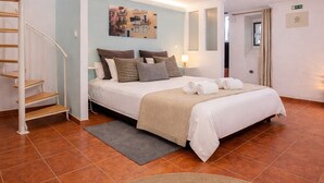 Una camera da letto con un letto, una scala, un'opera d'arte appesa al muro, una porta e un pavimento piastrellato.
