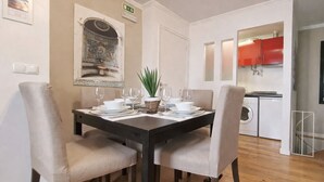 Zona pranzo con tavolo apparecchiato per quattro persone, due sedie per lato, un piccolo centrotavola con una pianta e un quadro appeso alla parete.