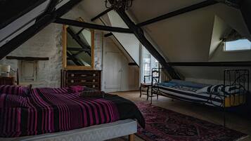 Ein Schlafzimmer mit schrägen Wänden, einem Bett mit gemustertem Überwurf, einer Kommode, einem Spiegel und einem Fenster.