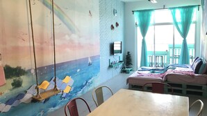Ein Zimmer mit einem Bett, einem Tisch, Stühlen, einem Fernseher und einem Wandgemälde.