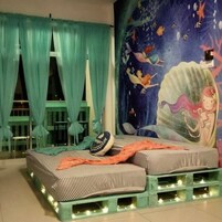 Una stanza con un letto con lenzuola a righe, un affresco di una sirena, tende color acquamarina e un tavolino con sedie.