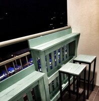 Un balcone con ringhiera verde e due tavolini.
