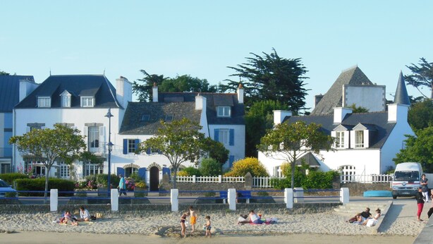 Une ville côtière aux bâtiments blancs, dotée d’une plage de sable et bordée d’une eau calme.