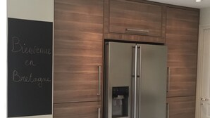Une cuisine moderne avec un réfrigérateur en acier inoxydable, des meubles de rangement en bois et un tableau noir fixé au mur.