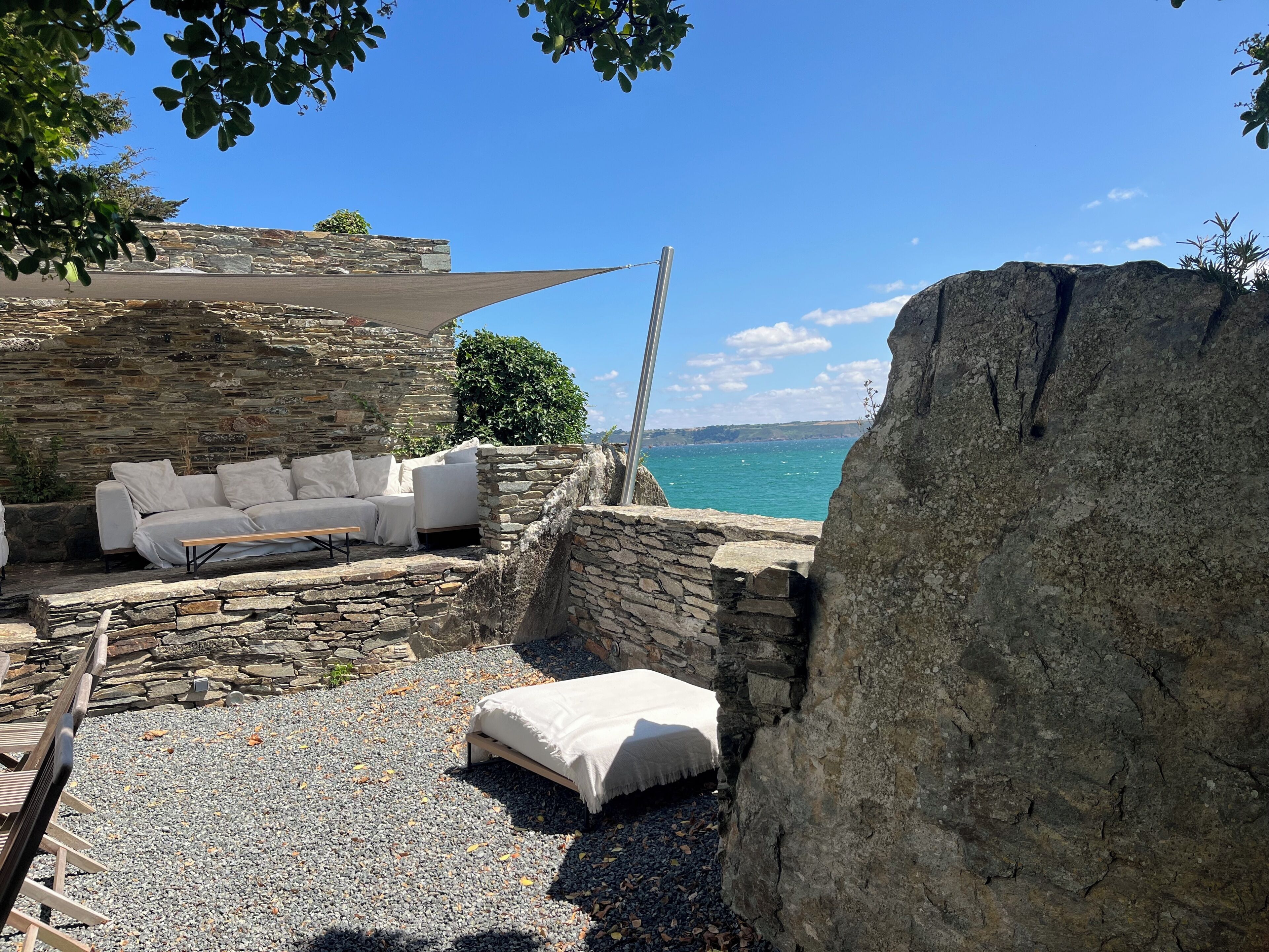 Un espacio al aire libre con paredes de piedra, un sofá blanco y una pequeña mesa, con vista a un cuerpo de agua.