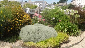 Un jardin avec différentes plantes et fleurs, une clôture blanche et des bâtiments en arrière-plan.