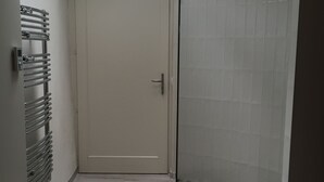 Un couloir étroit avec un puits de lumière, une porte, une douche avec un sol carrelé et un radiateur.