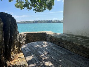 Un banc en pierre offrant une vue sur la mer, avec un arbre qui le surplombe.