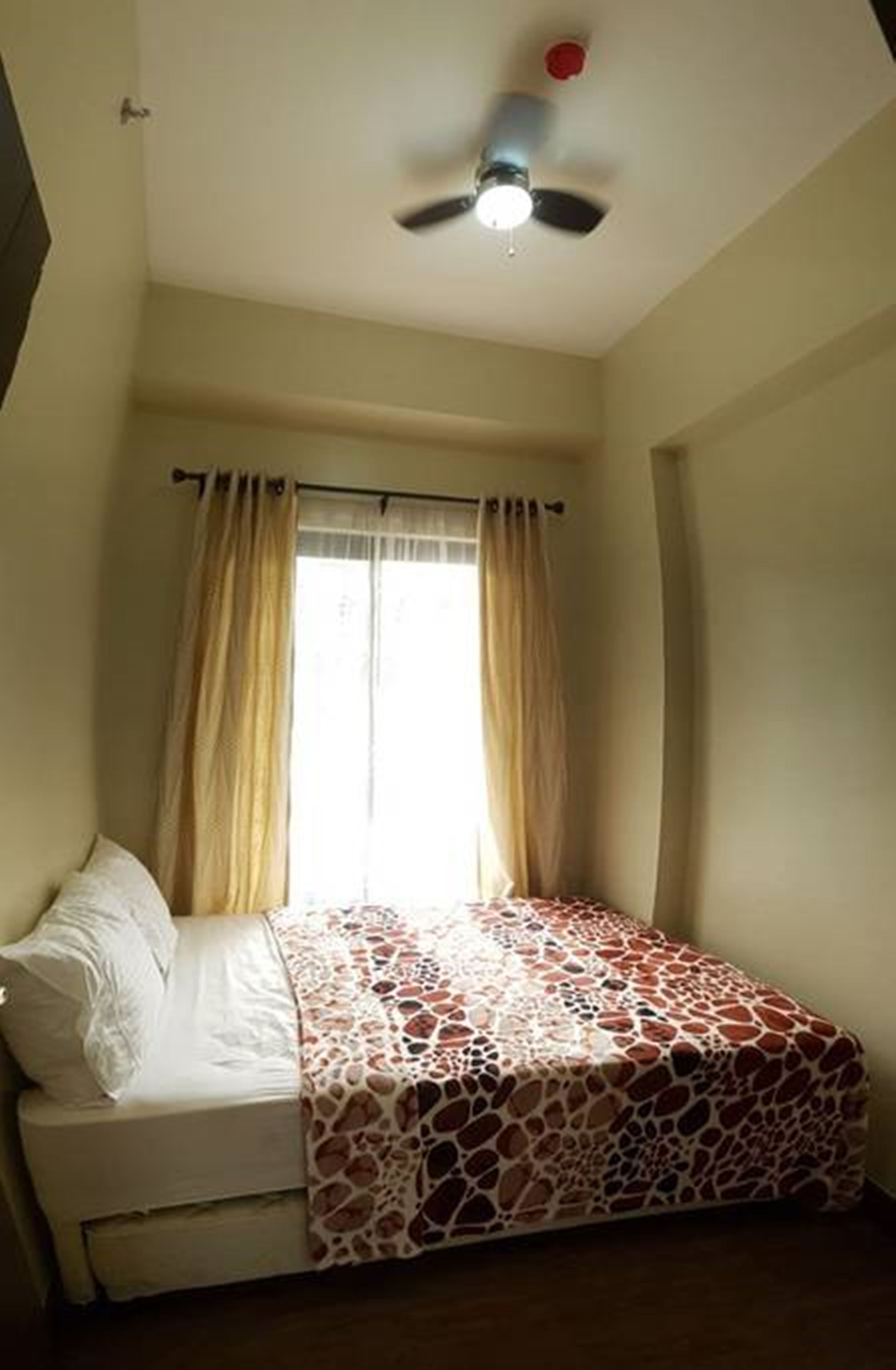 A bedroom with a bed, a ceiling fan, and a window with curtains.