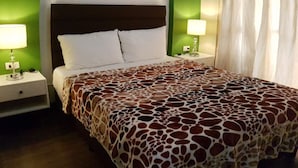 Habitación de hotel con cama, paredes verdes, ventilador de techo y mesita de noche con lámpara.