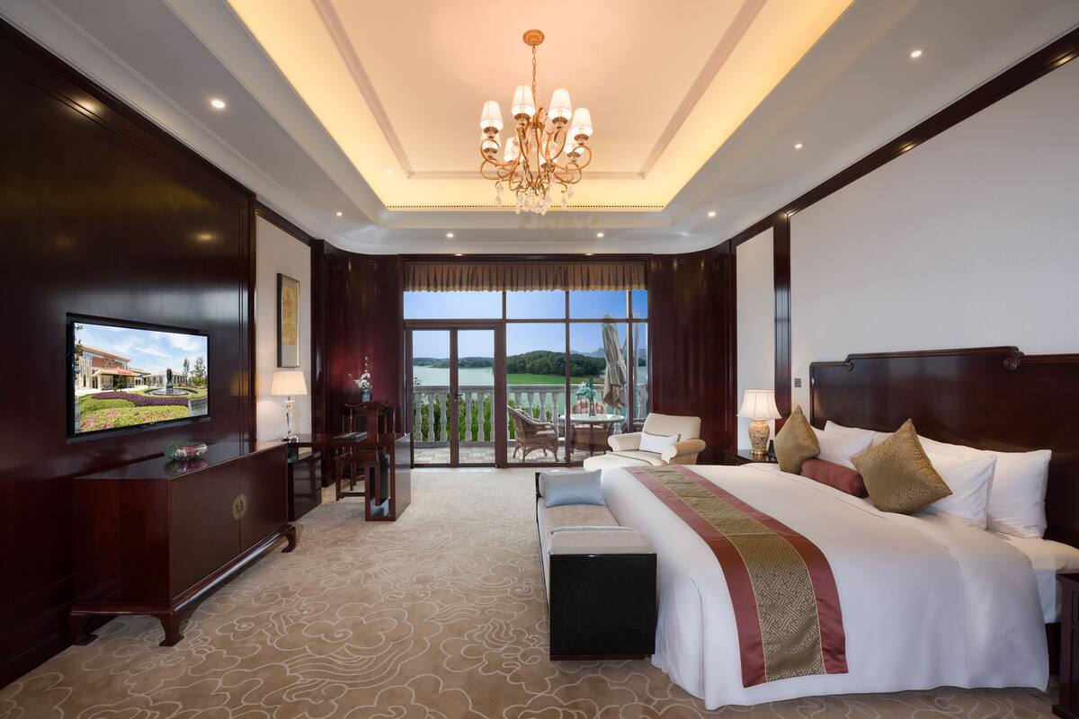 Een hotelkamer met een groot bed, een televisie, een balkon met uitzicht en een kroonluchter.