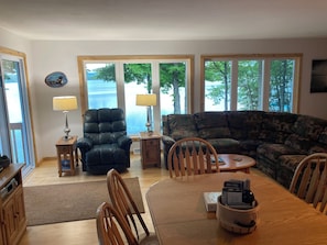 A living room with a leather chair, a sofa, a dining table with chairs, and large windows with a view of trees and a body of water. - Waterfront Lake House , Crane Lake, Pickerel WI. See our video! (Pickerel)