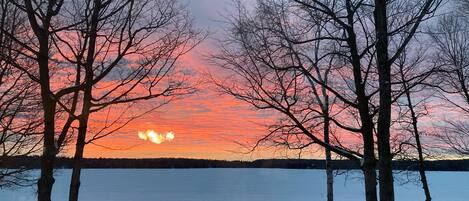 A view of a lake with trees in the foreground and a sunset in the background.
