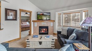 A cozy living room with a fireplace, a television mounted above it, and a comfortable seating area with a sofa and a coffee table. - Direct Unit Access,  Garage, 2 decks, Weber BBQ, Surround Sound Home Theater (Steamboat Springs)