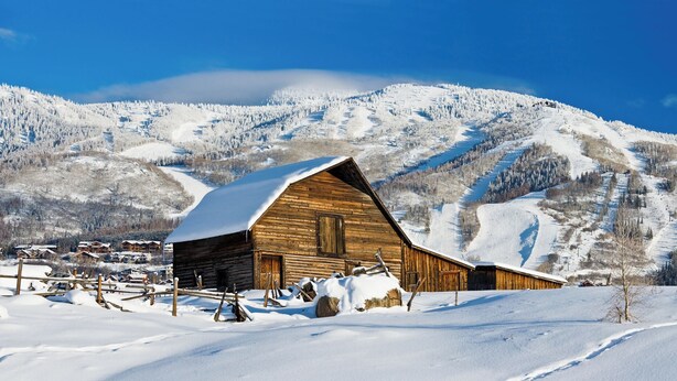 A wooden cabin with a sloped roof, surrounded by a snowy landscape and mountains in the background. - Direct Unit Access,  Garage, 2 decks, Weber BBQ, Surround Sound Home Theater (Steamboat Springs)