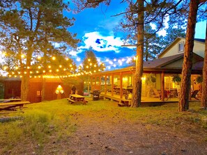 A rustic outdoor dining area with string lights, wooden tables, and a covered seating area. - Colorado Family Reunion and Wedding Headquarters (Jefferson County)